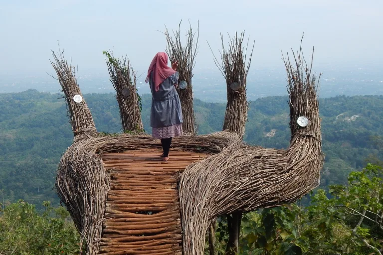 Seorang wanita menaiki spot foto Panca Wara di Hutan Pinus Pengger